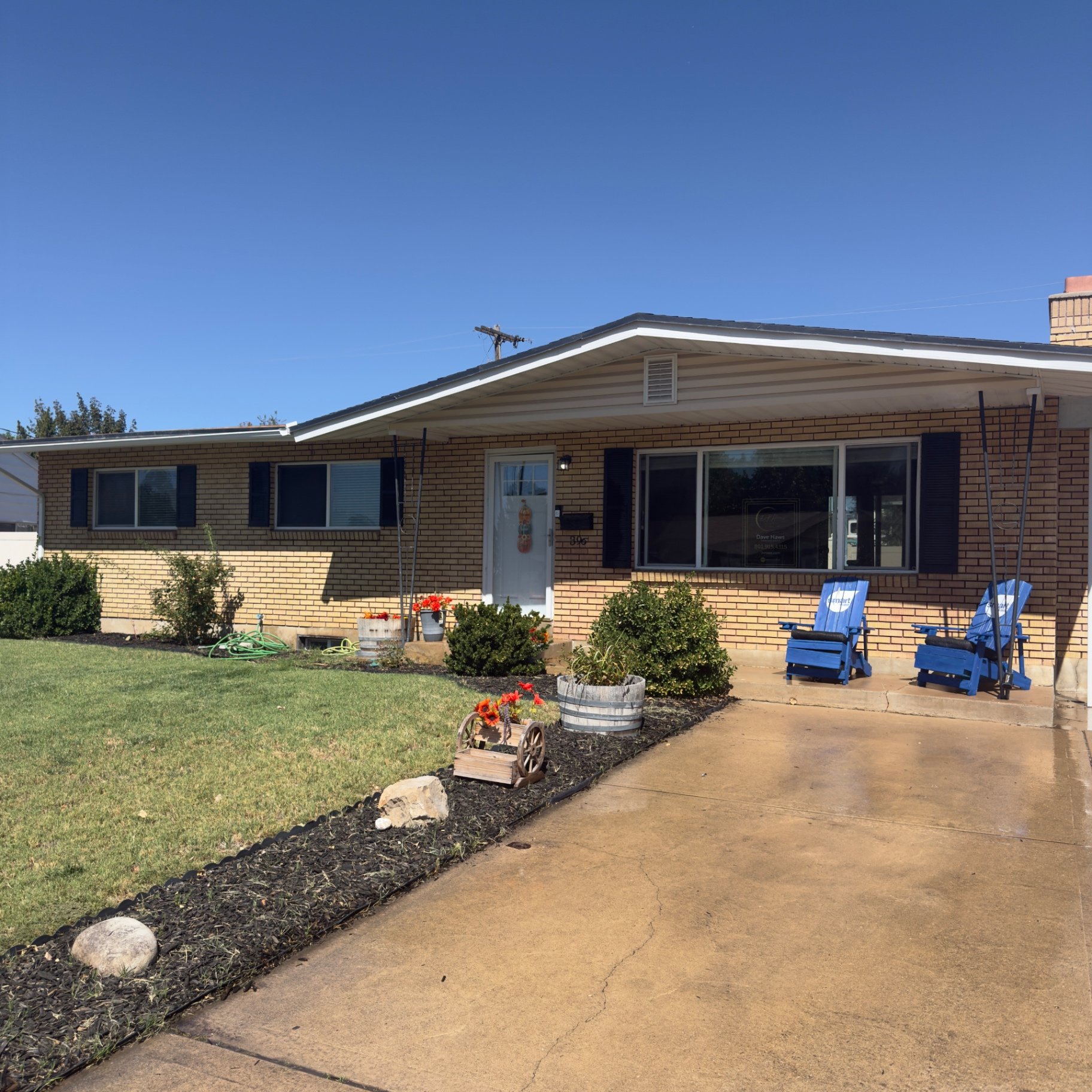 Front exterior of 396 W 1130 N with covered porch, blue chairs and flower planters — a 5 bedroom all-brick rambler in Sunset, Utah
